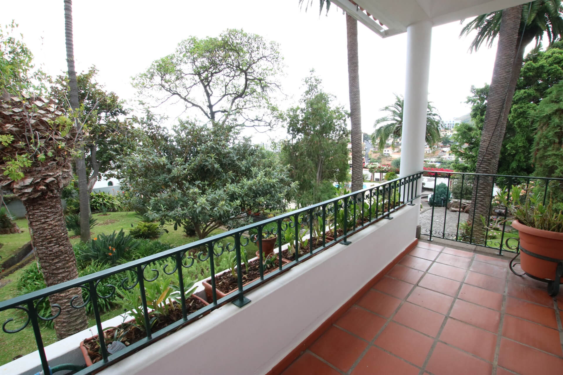 A veranda with an orange tiled floor, green rails and a view to the garden