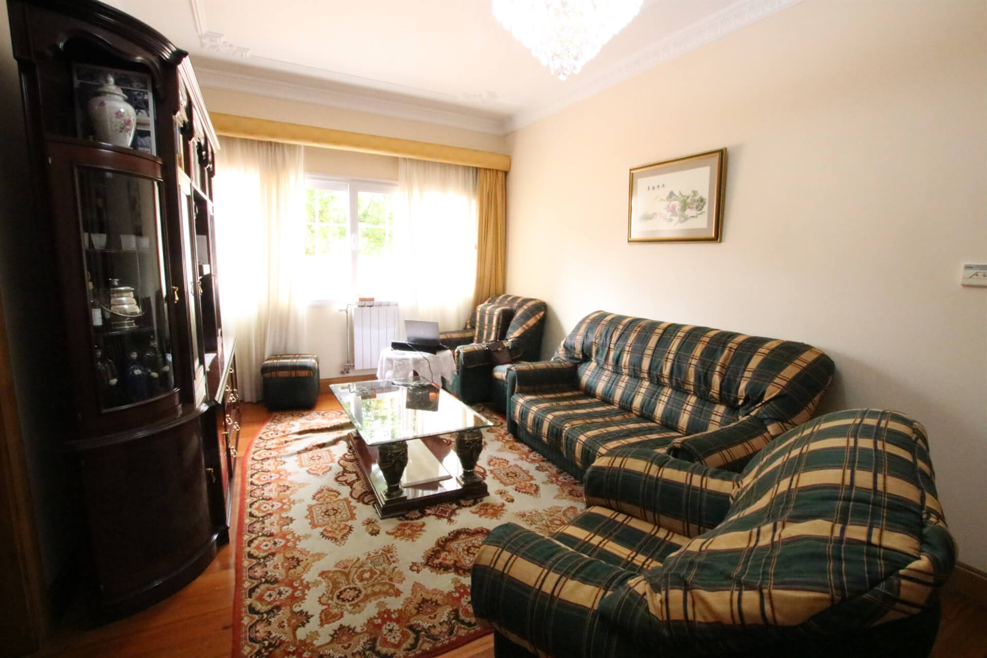 A lounge with 3 green and yellow sofas, a table, a cupboard and a painting on the wall