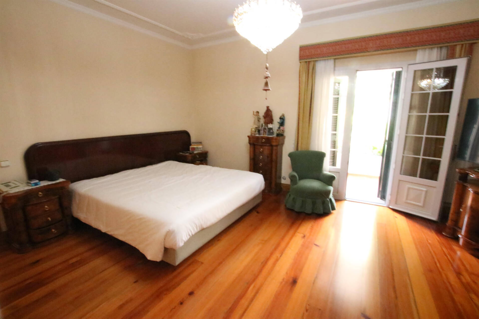 Bedroom with wooden floor, a bed and a chair with the veranda door open